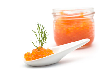 Fototapeta na wymiar Closeup of trout roe in a ceramic spoon with a dill leaf with a transparent glass container on white background