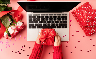 Female hands holding a red valentine gift box top view on pink background