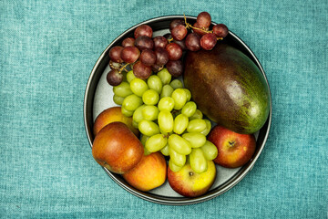 overhead shot of round fruit bowl with grapes, mango and apples