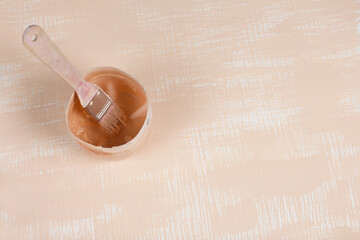 Tray with remnants of beige paint and paintbrush. On a surface painted in white and beige.