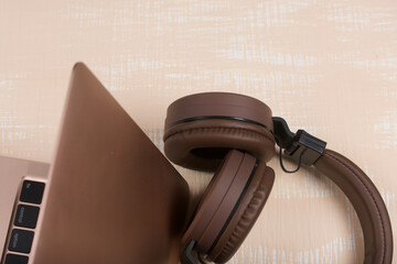 Fragment of an open pink laptop. Nearby are wireless headphones in brown. The surface is painted in white and beige.