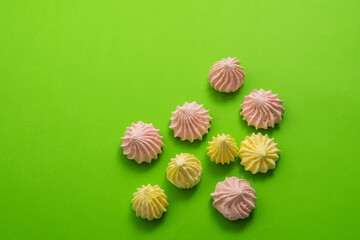 Colorful meringues lie on a green background. Bright sweets.