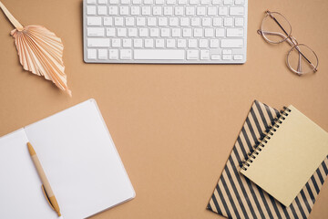 Women's workplace from above. Flat lay computer keyboard, blank paper notebook, glasses, notepad on brown background. Freelancer workspace, home office desk