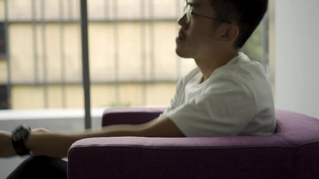 Asian Man sitting down on a purple chair for an interview and answering questions