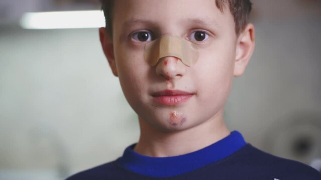 portrait of a child with a plaster on his nose. the boy who hurt his face. a wound on the nose and bruises with scratches on the face. satisfied with the treatment