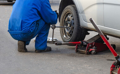 Obraz premium Mechanic screwing or unscrewing changing car wheel by wrench mechanic at work changing a wheel on a car