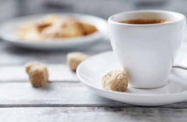 Cup of coffee and brown sugar cubes ( focus on sugar) on bright wooden background. Close up. 