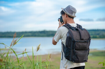 Young Asian man traveler with backpack taking a photo and looking at amazing lake. Travel holiday relaxation concept
