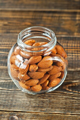 Almonds in a glass transparent jar. Nuts on an old shabby board. Jar on a brown wooden table close up.