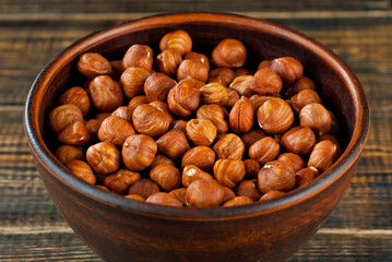 Hazelnuts in a clay bowl on an old shabby board. Nuts on a brown wooden table.