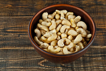 Cashews in a clay bowl on an old shabby board. Nuts on a brown wooden table.