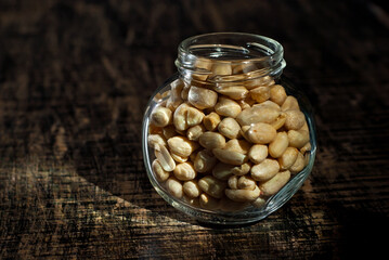 Peanuts in a glass transparent jar. Nuts on an old shabby board. Jar on a brown wooden table close...