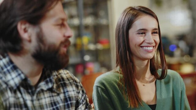Happy pretty caucasian girl with boiyfriend staying in company of friend chatting about lifestyle. Multi-ethnic friendly young people hanging out in cafeteria.