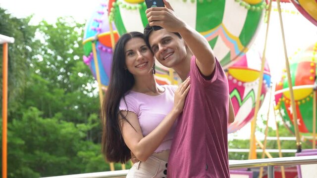 couple in love hugging , kissing and taking selfie by smartphone together at the amusement park outdoors in summer having fun in vacation