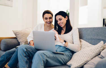 Cheerful female friends using laptop on sofa