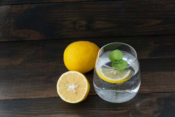 transparent glass with pure water, lemon slice, mint leaf ,  whole lemon and half of it lie near on...