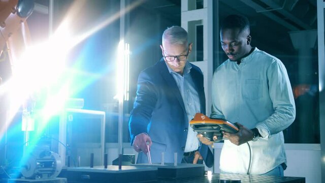 One engineer manages robot actions via controller, another one puts steel cylinders into the holes