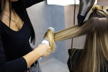 Naklejka premium Young hairdresser using hair dryer and comb to the hair of woman