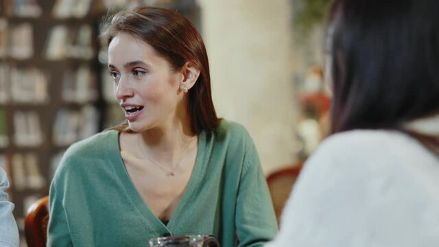 Young attractive caucasian woman communicating with multi-race haopy friends together sociializing reunion event in the cafe interiors. Casual meeting.