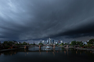 Naklejka na ściany i meble Thunderstorms and storms with weather phenomena over Frankfurt. Clouds over the skyline and the Main. Dramatic mood with skyline. Boot auf dem Fluss. 