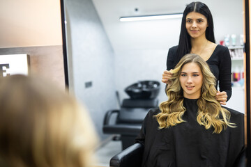 Hairdresser makes hairstyle close-up on blond hair of beautiful woman in saloon