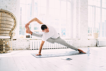 Young man practicing yoga Visvamitra pose in bright room