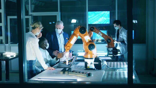 Engineers in masks working at robotics development laboratory. Innovation, technology concept.