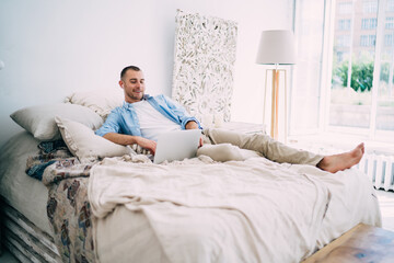 Positive young man relaxing in cozy bedroom