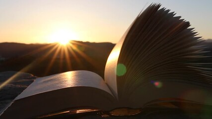 Pages of an open book moving in the wind with rays of sunlight at sunset or sunrise. Inspiration, creativity, reading, ideas and imagination concept. Poetic video.