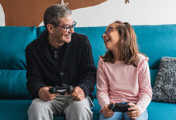Grandfather plays video games with his granddaughter in the living room.