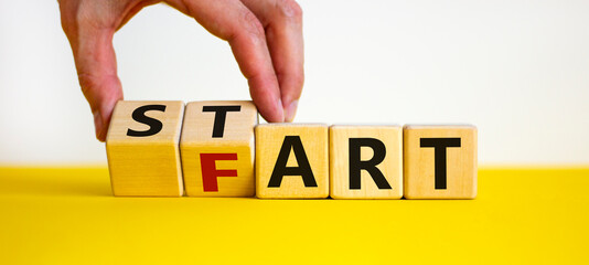 Good start or fart. Hand turns cubes and changes the word 'fart' to 'start'. Beautiful yellow table, white background. Business and fart or start concept. Copy space.