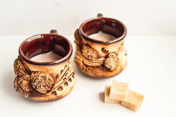 Small mugs with a beautiful design with a drink on a white background next to cubes of brown sugar