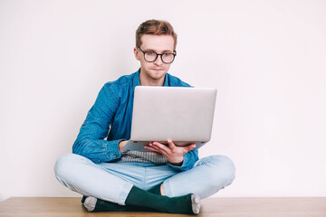 Young man in shirt and glasses working on laptop computer sitting on the table on a white background. Freelance work concept. Copy, empty space for text