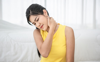 Young woman sitting on the bed after waking up in the morning and touching her aching neck.