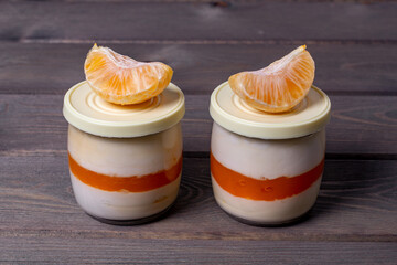 Creamy panna cotta with tangerine jelly in serving jars and fresh ripe tangerine on a wooden...