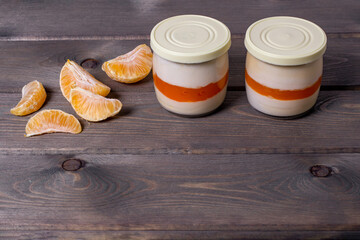 Creamy panna cotta with tangerine jelly in serving jars and fresh ripe tangerine on a wooden...
