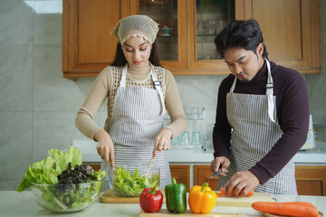 Happy Asian couple cooking together. Husband and wife in their kitchen at home preparing healthy vegetable food.