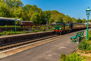 Obraz premium A train approaching a station on a railway line in the UK on a sunny summer day