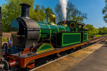 A train letting off steam before moving off on a railway line in the UK on a sunny summer day