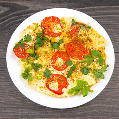cooked fried omelet with herbs and vegetables in a white plate on a wooden table