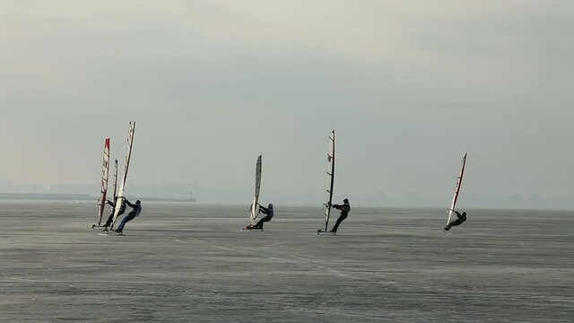 group of extreme athletes windboarders, glide under sail on the frozen sea ice