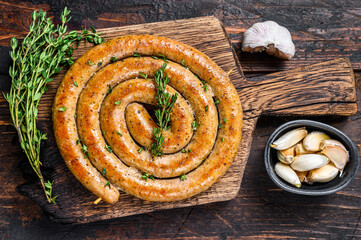 BBQ spiral sausage from pork and beef meat on a wooden cutting board. Dark wooden background. Top...