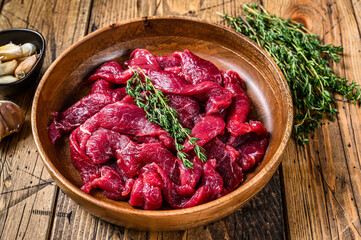 Raw uncooked beef meat sliced in strips with fresh herbs for beef stroganoff. wooden background....