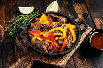 Fajitas beef meat traditional Mexican food dish in a pan. Dark wooden background. Top view