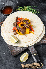 Mexican Fajitas with colored pepper and onions, served with tortillas and salsa. Black background. Top view