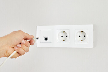 Male hand puts network plug in the socket. Close-up of a man hand plugging an ethernet cable into a wall socket.