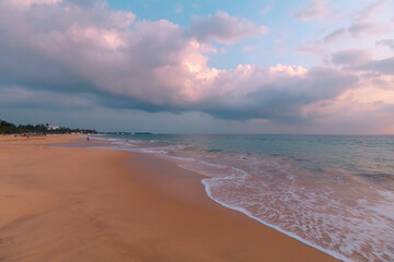 Beautiful ocean beach at sunset. Foamy waves over wheat sand and a beautiful cloudy sky.
