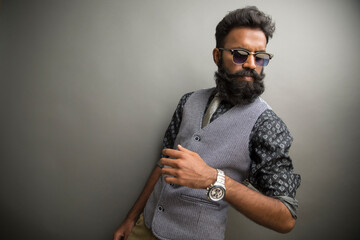 Bearded young businessman posing with sunglasses on gray.