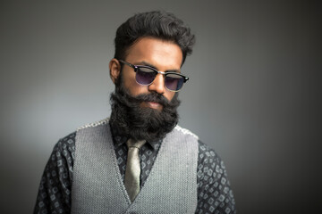 Bearded young businessman posing with sunglasses on gray.