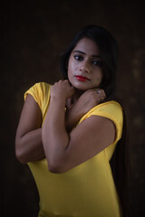 Studio portrait of a beautiful and young Indian Bengali female model in yellow tee shirt and jeans...